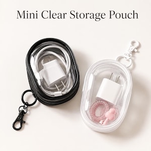 May include: Two mini clear storage pouches with the text Mini Clear Storage Pouch. One pouch is black with a black lobster clasp, containing a white power adapter and cable. The other is white with a white lobster clasp, containing a white power adapter, a pink spiral hair tie, and a small pink charm.