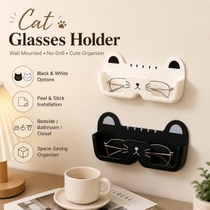May include: Two wall-mounted cat glasses holders, one white and one black, each featuring a feline face design with ears and whiskers. The holders are designed for peel and stick installation and are shown holding pairs of spectacles.