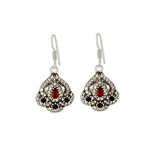 May include: A pair of silver dangle earrings with a red stone in the center of each earring. The earrings are decorated with small white stones.