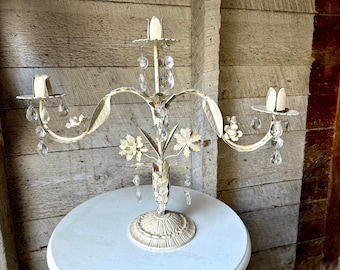 May include: White metal candelabra with three candle holders and crystal drops. The candelabra is decorated with floral details and has a white base.