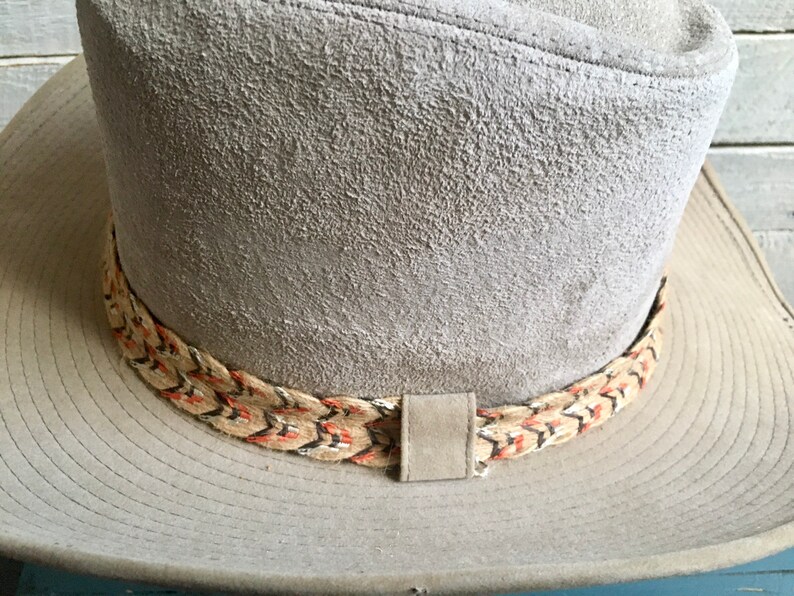 May include: A gray suede cowboy hat with a braided band featuring red, black, and white accents.