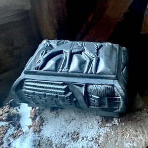 May include: A black wooden box with a carved design of a camel on the top. The box is sitting on a wooden surface.