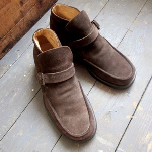 May include: A pair of brown suede ankle boots with a buckle strap. The boots have a pointed toe and a low heel.