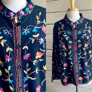 Könnte beinhalten: Eine schwarze bestickte Jacke mit bunten Blumenmustern. Die Jacke hat einen Stehkragen und einen Knopfverschluss.