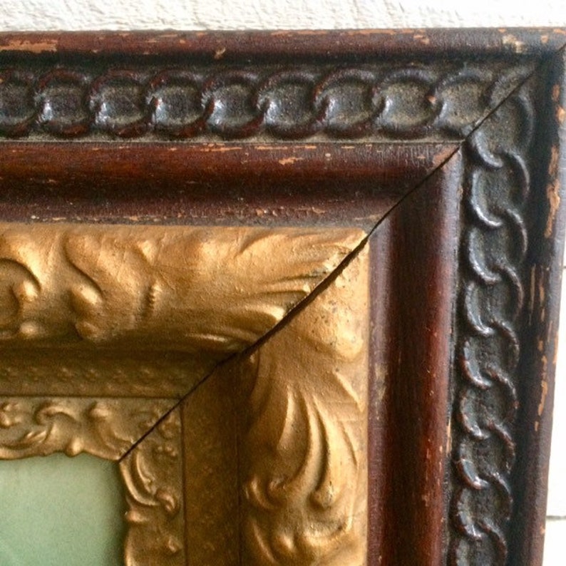 May include: Close-up of a wooden picture frame with a gold-painted inner edge. The frame has a decorative pattern and a dark brown finish.