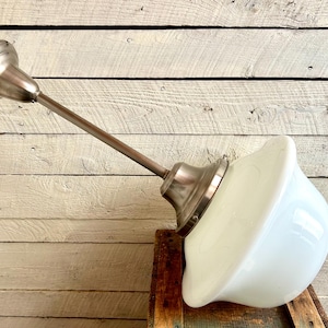 May include: Vintage-style pendant light with a white glass shade and brushed nickel finish. The light fixture has a long, angled arm and a bell-shaped shade, perfect for a kitchen or dining area.