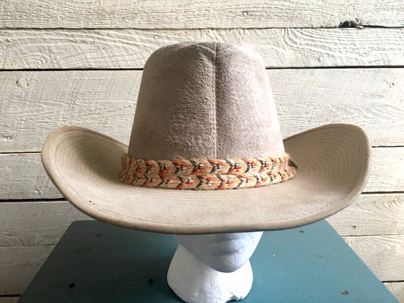 May include: A light brown cowboy hat with a woven band featuring orange, black, and white accents.