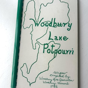 May include: A vintage cookbook titled "Woodbury Lake Potpourri" with a green spiral binding. The cover features a green outline of a lake and the text "Woodbury Lake Potpourri" in a handwritten font. Additional text includes "recipes compiled by Woodbury Lake Association, Woodbury, Vermont 1982."
