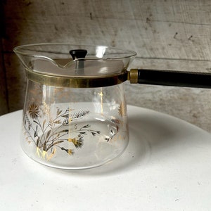 May include: A clear glass coffee pot with a black handle and gold floral design. The pot has a lid with a small knob.