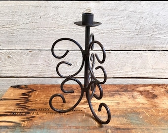 May include: Black metal candle holder with a decorative, swirling design. The holder has a single candle cup.