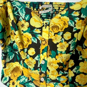 May include: A floral print top with yellow roses, green leaves, and a black background. The top has a square neckline, button-up front, and a smocked back. The tag reads "ASHLEY & URBAN OUTFITTERS".