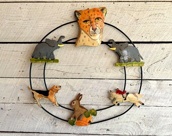 May include: A black metal wreath with wooden animal cut-outs. The wreath features a cheetah, two elephants, a rabbit, and a dog. The animals are painted in realistic colours.
