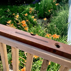 May include: A vintage wooden level with a brown finish. The level has a groove for a spirit level and a hole in the center. The level is resting on a wooden railing.