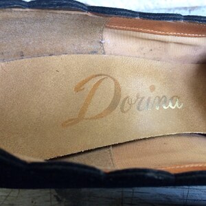 May include: Close-up of the inside of a black shoe with a brown leather insole. The insole is stamped with the word "Dorina" in gold lettering.