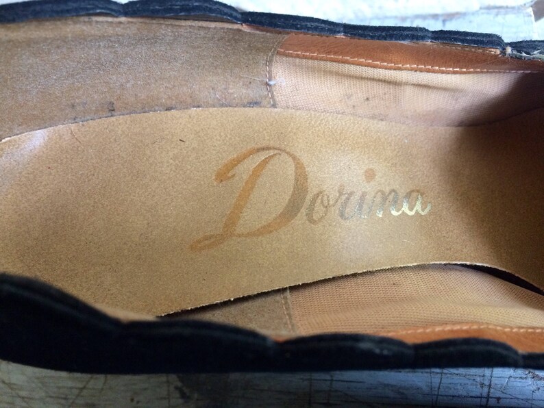May include: Close-up of the inside of a black shoe with a brown leather insole. The insole is stamped with the word "Dorina" in gold lettering.