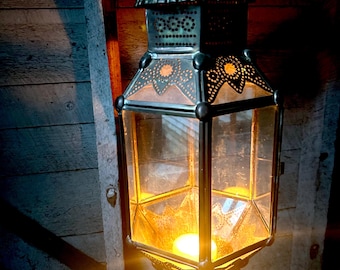 Puede incluir: Una linterna de metal decorativa con diseños intrincados y un panel de vidrio, iluminada por una cálida luz de vela.