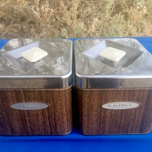 Puede incluir: Dos botes de metal vintage con tapas de madera. Los botes están etiquetados con "té" y "café".