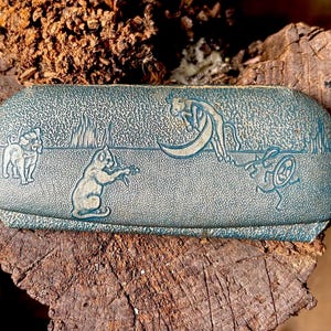 May include: A blue and white eyeglass case with a whimsical design featuring a dog, a cat, and a bird. The case has a textured surface and a subtle sheen.