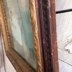 May include: A vintage framed portrait of two children, a girl and a boy, wearing matching blue outfits. The frame is made of wood with a gold-painted trim and a dark brown outer edge.