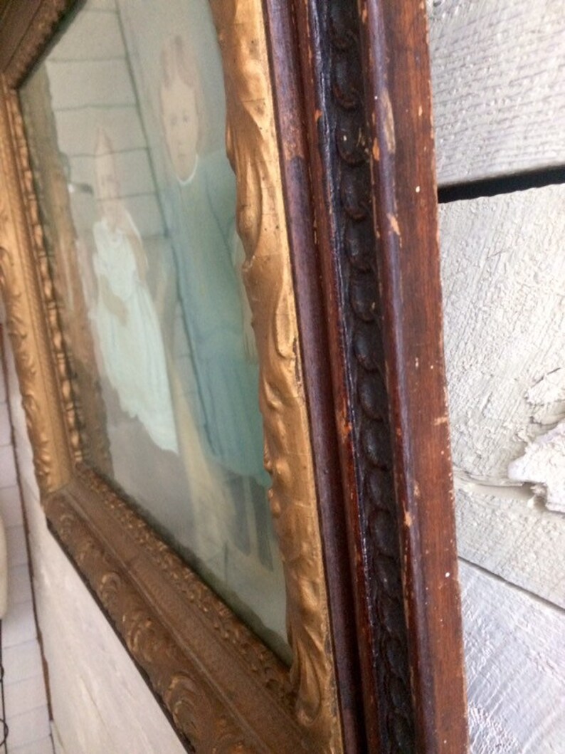 May include: A vintage framed portrait of two children, a girl and a boy, wearing matching blue outfits. The frame is made of wood with a gold-painted trim and a dark brown outer edge.