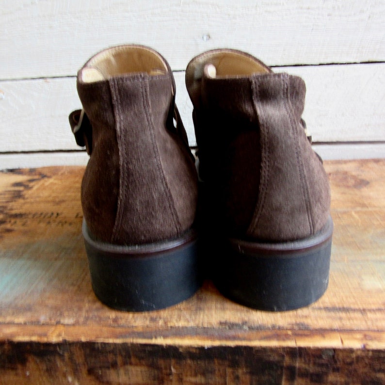 May include: A pair of brown suede ankle boots with a buckle closure. The boots have a thick rubber sole.