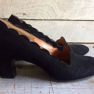May include: Black suede heels with a scalloped edge and a low block heel.