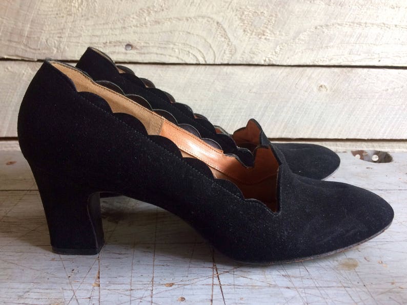 May include: Black suede heels with a scalloped edge and a low block heel.