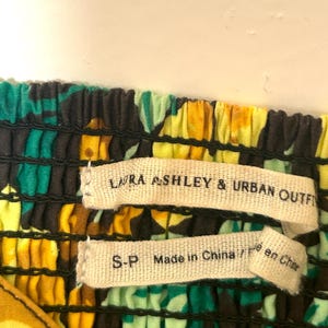 May include: Close-up of a colorful floral fabric with the labels "LAURA ASHLEY & URBAN OUTFITTERS" and "S-P Made in China / Fait en Chine". The fabric features a pattern of yellow, green, and black.