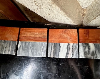 May include: Four rectangular coasters with a two-tone design. The top half is a warm, reddish-brown wood, while the bottom half is a grey and white marbled stone. The coasters are arranged in a row.