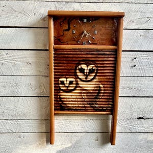 Puede incluir: Un lavadero de madera con una esfera de reloj y una imagen pintada de dos búhos. El lavadero es marrón y los búhos son blancos con ojos negros.