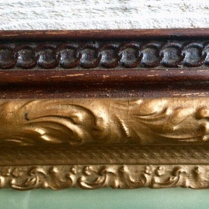 May include: Close-up of a gold-colored ornate picture frame with a dark brown wood inner frame. The frame has a decorative, intricate design.