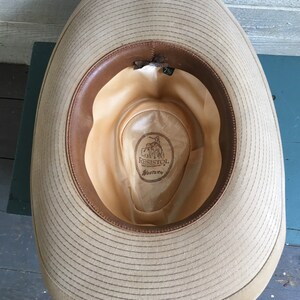 May include: The inside of a tan cowboy hat with a brown leather band. The hat is labeled "Resistol Western" and has a size tag of "7 1/8".