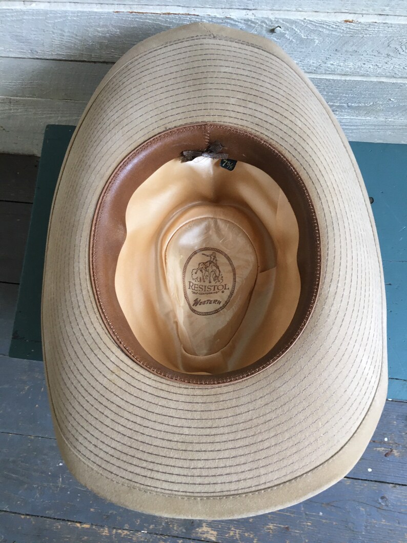 May include: The inside of a tan cowboy hat with a brown leather band. The hat is labeled "Resistol Western" and has a size tag of "7 1/8".
