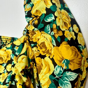 May include: Close-up of a floral print top featuring large yellow roses, green leaves, and brown accents on a black background. The top has a square neckline and puffed sleeves, with elastic detailing.