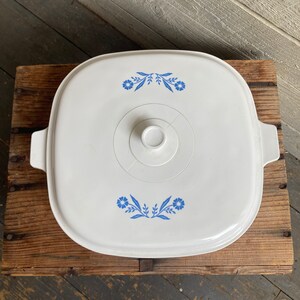 May include: White square baking dish with a blue and white floral design. The dish has a lid with a knob in the center.