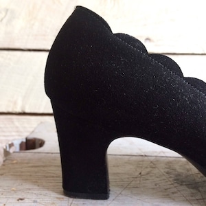 May include: Black suede heeled shoe with a scalloped edge and a chunky heel.