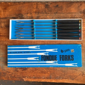 Könnte beinhalten: Eine blaue Box mit weißem Rand, die sechs Fondue-Gabeln aus Edelstahl mit schwarzen Griffen und farbigen Spitzen enthält. Die Box trägt den Text "6 Stück" und "Fondue Forks".