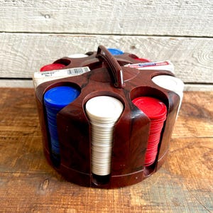 May include: A brown plastic poker chip holder with a handle. The holder has six compartments, each filled with stacks of poker chips. The chips are red, white, and blue.