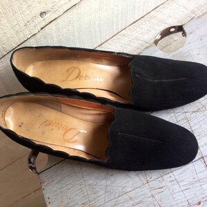 May include: A pair of black suede shoes with scalloped edges. The shoes have a pointed toe and a low heel. The brand name "Dorina" is visible on the inside of the shoes.