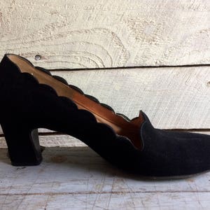 May include: Black suede heeled shoes with a scalloped edge detail.