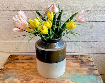 Könnte beinhalten: Ein Strauß gelber und rosa Tulpen in einer braunen und weißen Keramikvase. Die Vase hat einen braunen oberen Teil und einen weißen unteren Teil. Die Vase steht auf einem Holztisch.