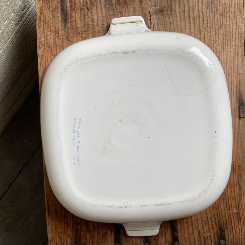 May include: White ceramic baking dish with two handles. The bottom of the dish has the text "PYROCERAM Made in U.S.A. 10" x 14" Oven to Tableware"