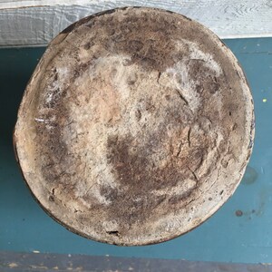 Puede incluir: La parte inferior de una gran olla de cer&aacute;mica redonda con un esmalte marr&oacute;n. La olla tiene una superficie rugosa y texturizada y muestra signos de desgaste y edad.