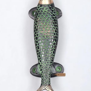 May include: A metal door handle shaped like a fish with a polished brass head and tail. The body features a dark black finish with green highlights on the raised scale texture. It includes two mounting plates with screw holes at the top and bottom.