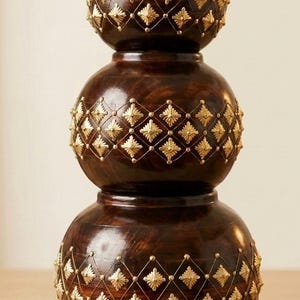 May include: A dark brown wooden vase with a stacked, three-tiered spherical shape. The surface is decorated with a gold-colored wire grid pattern, featuring small gold star-shaped accents at each intersection of the diamond-shaped grid.