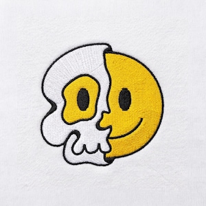 May include: An embroidered patch on a white fabric background featuring a split design. The left side is a white skull with a yellow eye socket, while the right side is a yellow smiley face with a black eye and a curved black mouth outline.