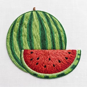 Può includere: Una toppa ricamata a mano raffigurante un'anguria intera con strisce verticali verde chiaro e scuro, abbinata a una fetta di anguria rosso brillante con semi neri a forma di goccia, il tutto cucito su uno sfondo di tessuto bianco.