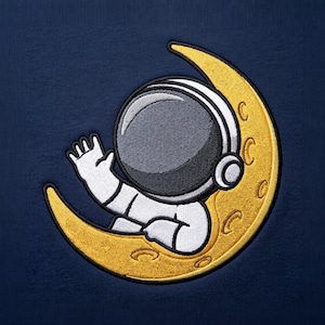 May include: An embroidered patch on a dark blue fabric background featuring a yellow crescent moon and a white astronaut suit with a dark gray helmet visor. The astronaut is depicted waving a hand while positioned within the curve of the moon.
