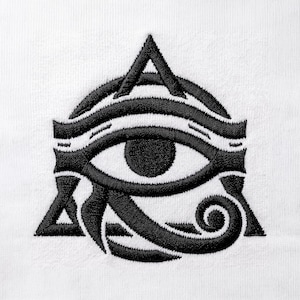 May include: A black embroidered Eye of Horus symbol stitched onto a white fabric background. The design features the iconic ancient Egyptian ocular motif with its characteristic curved lines, a central pupil, and a triangular base structure.