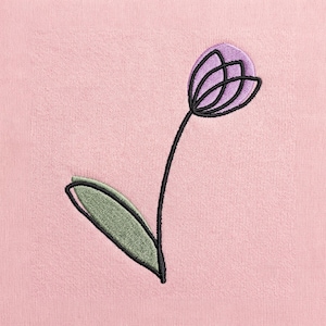 May include: A light pink fabric featuring a minimalist machine embroidery design of a single tulip. The flower head is filled with light purple thread, while the stem and leaf are outlined in black, with the leaf filled in sage green.